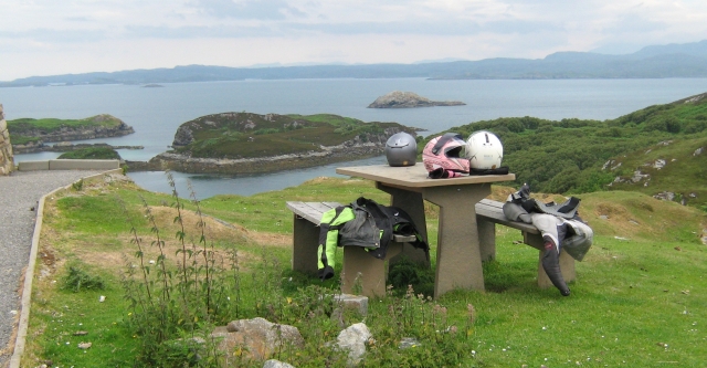 bike helmets and jackets on a bench with islands and mountains at drumbeg viewpoint